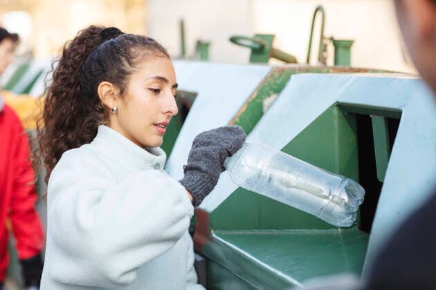 IMAGO Creative: Klimawandel - Umwelterziehung Smiling female environmentalist with friend throwing plastic bottle in garbage can Sweden, Stockholm, model released Copyright: xMaskotx , MA81932