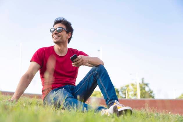 IMAGO Creative, Lifestyle, Frühling in der Stadt Attractive young man dressed with red t-shirt smiling in the park with sunglasses and smartphone Copyright: xJosxTempranox Model Released