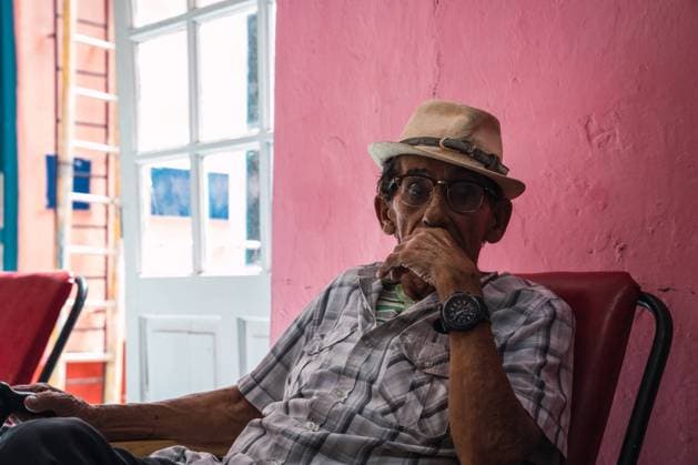 IMAGO Creative: NGO, Rehabilitation und Gesundheitswesen LA HABANA, CUBA - NOVEMBER, 6 , 2018: Elderly Hispanic male in eyeglasses and hat sitting near pink wall in Cuba Copyright: xKikexArnaizx Model Released