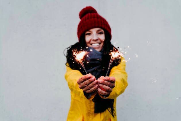 Smiling woman holding sparkler while standing against gray wall model released Symbolfoto EBBF01279