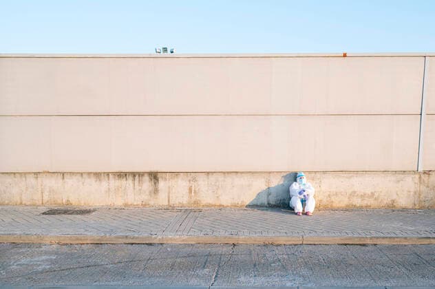 Nurse wearing protective suit sitting on footpath against wall model released Symbolfoto PGF00125