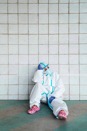 Contemplating female nurse with head in hands sitting against tiled wall model released Symbolfoto PGF00131