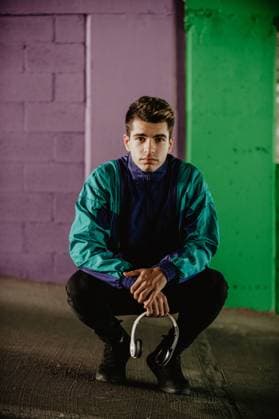 IMAGO Creative: Sport Start-Up Handsome man in sport jacket with headset in hand sitting near purple and green wall of building and looking at camera, Model released Copyright: xLuciaxVargasx MR
