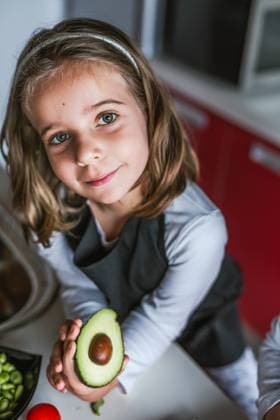 Little girl demonstrating half of ripe avocado to camera while standing in the kitchen looking at camera, Model released Copyright: xLuisxManuelxMatiasx MR