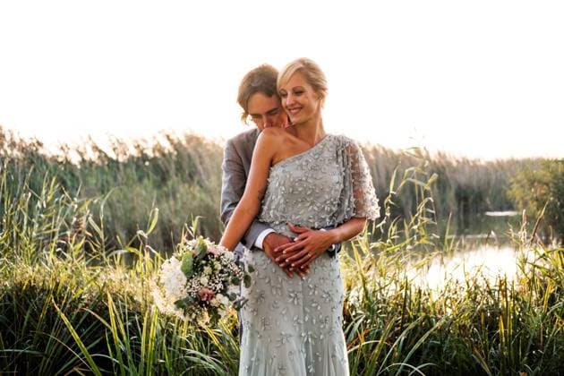 Stylish newly married couple in wedded suits embracing and kissing with green plants and mere on sunny day, Model released Copyright: xManuelxOrtsx MR