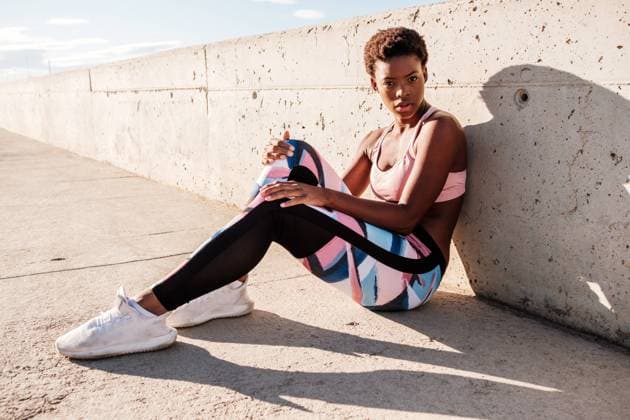 IMAGO Creative: Sport in der Stadt African American female athlete in flowered sport clothes and white sneakers looking at camera while sitting alone on concrete wall in sunbeams and resting after training in city, Model released Copyright: xManuelxOrtsx MR