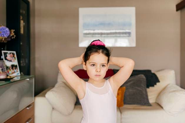 Adorable upset little girl dancer in leotard looking away while doing hair bun before ballet training in cozy living room at home Copyright: xManuelxRuizxAlbax Model Released