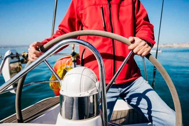 Crop unrecognizable man in red jacket and jeans standing at steering wheel while sailing in sea on modern vessel Copyright: xManuelxRuizxAlbax Model Released