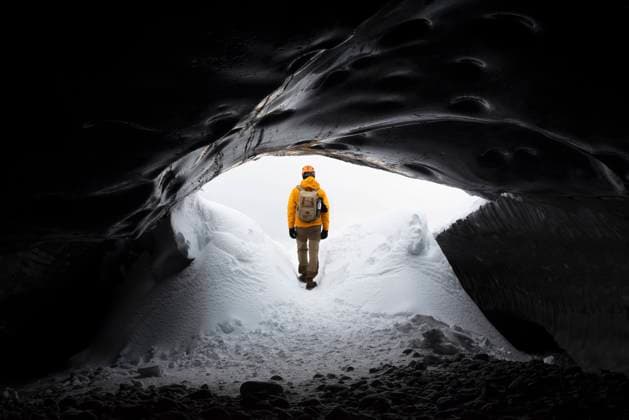 Remote anonymous explorer in warm clothes entering dark snowy cave in cold weather on winter day, Model released Copyright: xMarinaxTobaruelax MR