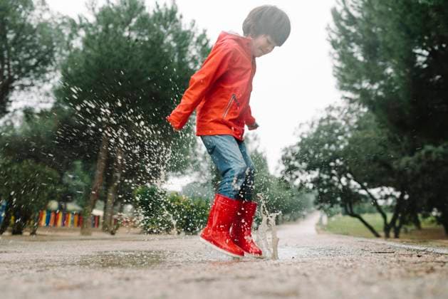 IMAGO Creative: Ruhe im Chaos Adorable joyful child in red raincoat and rubber boots having fun jumping in puddle on street in park in gray day, Model released Copyright: xMartaxMachinx MR