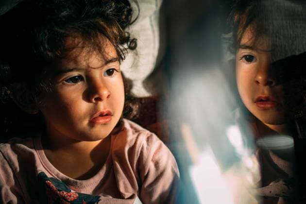IMAGO Creative: Gesundheit, Stille Curious kid with curly hair sitting near illuminated glass while resting at home at night Copyright: xPatriciaxBecarotox Model Released