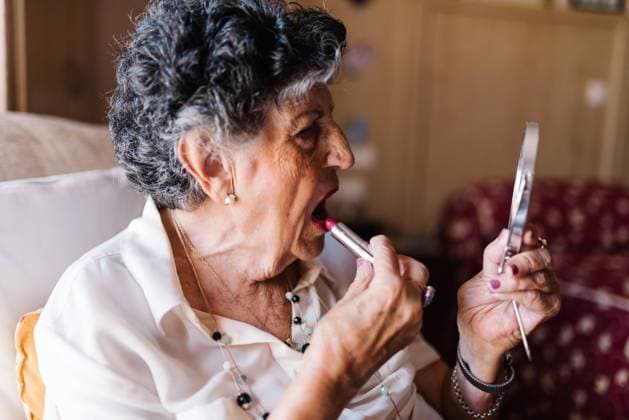IMAGO Creative: Clickbait, Hautpflege und Kosmetik Aged gray haired female applying lipstick while looking in mirror and sitting on armchair at home, Model released, Property released Copyright: xPatriciaxBecarotox MR