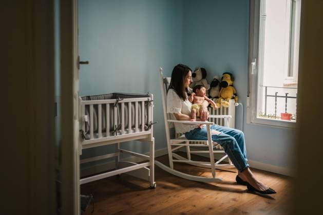 IMAGO Creative: Gesundheit, Stille Side view of beautiful woman holding cute baby and sitting on rocking chair near bassinet in cozy nursery Copyright: xPatriciaxBecarotox Model Released