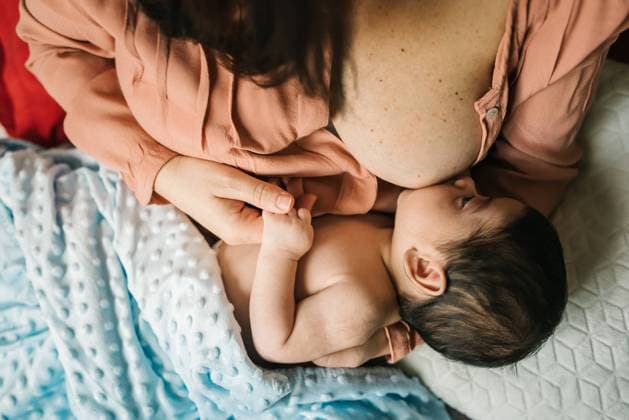 IMAGO Creative: Internationaler Frauentag, Mental Load und Care-Arbeit From above faceless mother holding on hands and breastfeeding newborn baby wrapped in blanket on bed at home Copyright: xPatriciaxBecarotox Model Released