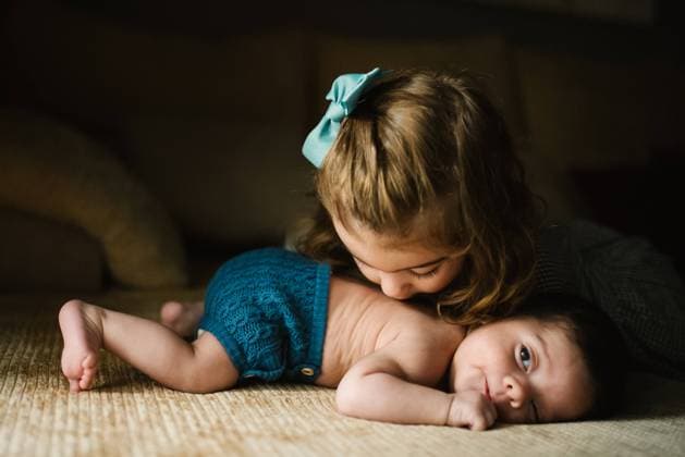 IMAGO Creative: Neue Aussichten brunette sister kissing the back of little baby looking away at home Copyright: xPatriciaxBecarotox Model Released