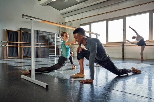 Cheerful interracial couple of professional ballet dancers training near big windows in a modern studio using wooden handrail, Model released Copyright: xPhilippexDegrootex MR