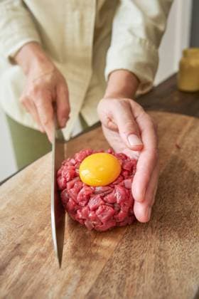 From above of unrecognizable female chef cooking Steak tartare in kitchen while making round shape of raw beef with egg yolk, Model released Copyright: xPhilippexDegrootex MR