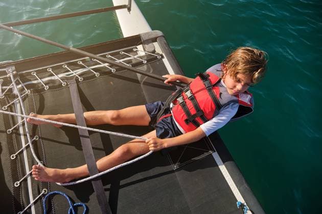 Aerial photo of a blond boy with life jacket leaning on the edge of a boat holding the rudder and a rope with the shore far away in the background, Model released Copyright: xPhilippexDegrootex MR