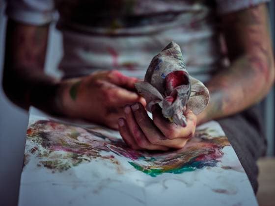 Crop pretty creative boy in casual clothes smeared in colorful paints sitting on chair and holding brush and napkin Copyright: xPhilippexDegrootex Model Released