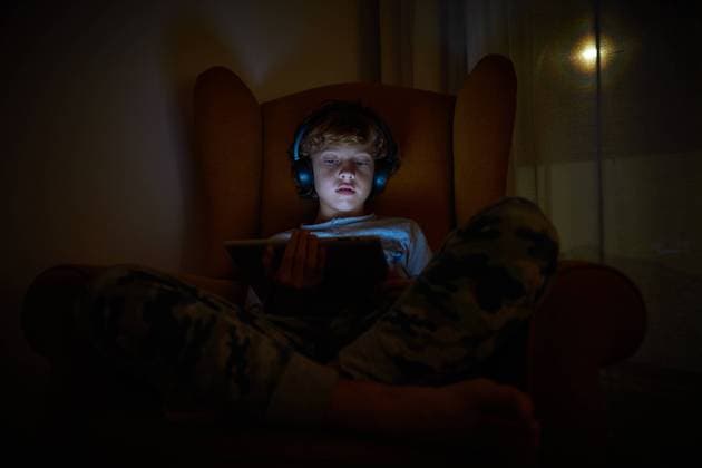 IMAGO Creative, Jahreszeit Herbst, Ferien Stock photo of a child sitting in an armchair in a corner of a room with a tablet on his lap with headphones at night. Technology Copyright: xPhilippexDegrootex Model Released