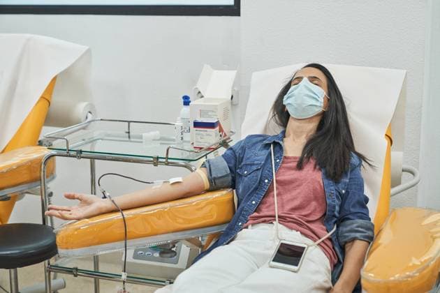IMAGO Creative: Zivildienst und ehrenamtliches Engagement From above of relaxed young female in protective mask with smartphone sitting in medical chair during blood donation in modern hospital Copyright: xPhilippexDegrootex Model Released