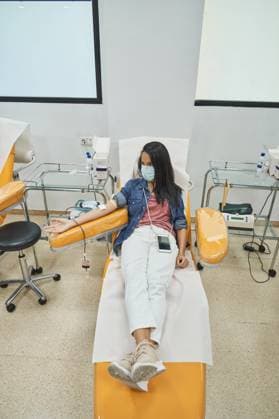 IMAGO Creative: Zivildienst und ehrenamtliches Engagement woman in protective mask sitting in medical armchair during blood transfusion procedure in contemporary hospital Copyright: xPhilippexDegrootex Model Released