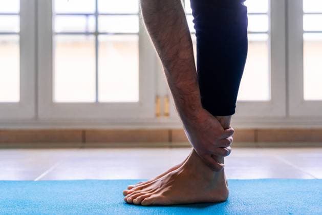IMAGO Creative: Kulturelle Folgen der Pandemie: Gesundheitsbewu?tsein und Alleinsein Low angle side view of unrecognizable flexible barefoot man in sportswear doing standing forward bend exercise while training alone on sports mat against window in light spacious room at home Copyright: xPolxSolex Model Released