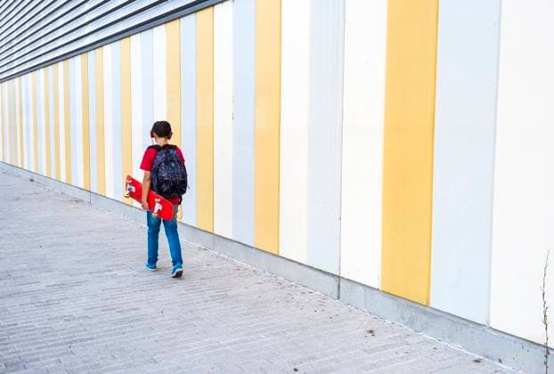 IMAGO Creative: Stadt-Dichotomien View of a young boy wearing casual clothes walking against a colored wall while holding a skateboard Copyright: xRafaxFernandezx Model Released
