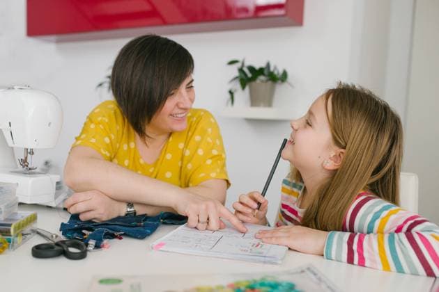IMAGO Creative: Gesellschaft, Integration IMAGO Creative: Internationaler Frauentag, Mental Load und Care-Arbeit Happy adult woman smiling and helping girl with homework assignment while sewing garment at home Copyright: xRamonxLopezx Model Released
