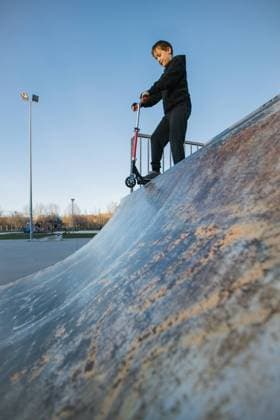 IMAGO Creative, Lifestyle, Frühling in der Stadt From below of active teen boy in protective helmet with kick scooter standing on ramp in skate park while preparing for performing trick in sunny spring day Copyright: xRamonxLopezx Model Released