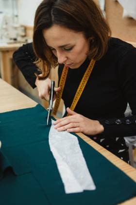 IMAGO Creative: Kreative Renaissance -- der junge Entrepreneur Unrecognizable woman using sharp scissors to cut garment detail from fabric while sitting at table in tailor workshop Copyright: xRaquelxArocenax Model Released