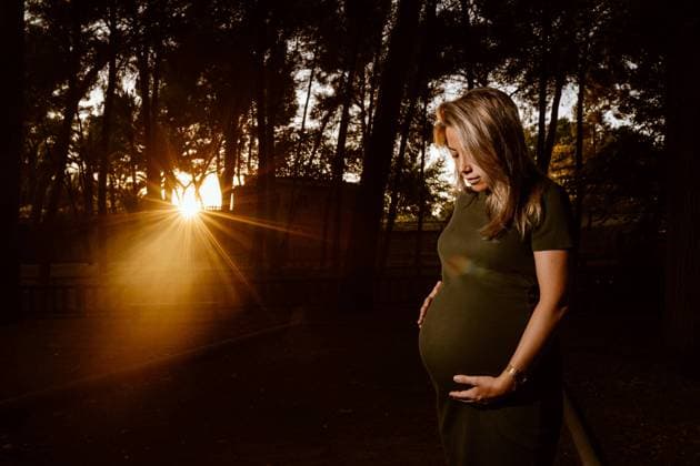 Happy pregnant woman in casual dress stroking belly while standing on pathway in park with green trees in sunny summer day with blue sky, Model released Copyright: xSantixMiquelx MR