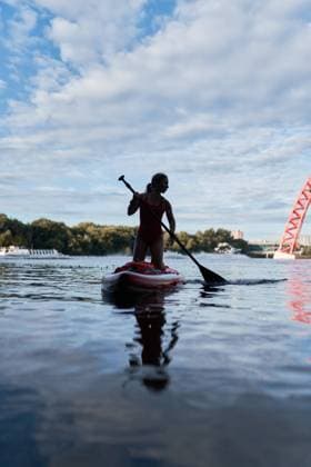 IMAGO Creative, Jahreszeit Sommer, Sommer in der Stadt Front view of woman standing on paddle board in river and rowing with paddle under bridge in city Copyright: xSergeyxMironovx Model Released