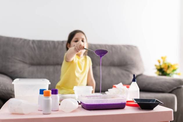 IMAGO Creative: Clickbait, Deko Ideen f?r Zuhause Child in yellow t shirt with spoon adding purple substance into rectangular plastic container while preparing blend and sitting on couch in living room Copyright: xSergioxVictorxVegax Model Released