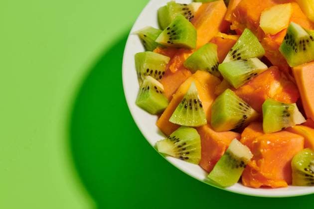 Closeup of delicious healthy natural fruit salad with chopped papaya and kiwi served in plate placed on bright green background Copyright: xSixAndxSix Model Released