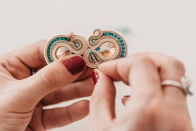 Closeup of crop skilled craftswoman creating soutache bijouterie with threads and beads in bright workshop, Model released Copyright: xSixAndxSix MR