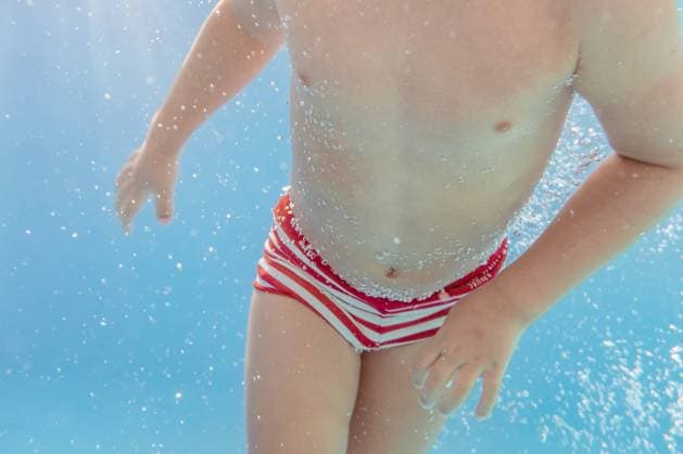 Underwater view of cropped unrecognizable kid swimming in clear water of pool and looking at camera Copyright: xSixAndxSix Model Released