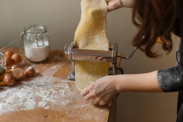 Faceless woman rolling out pastry with pasta machine while cooking delicious dinner with flour and kitchen utensils on wooden table at home Copyright: xValeriaxSchettinox Model Released