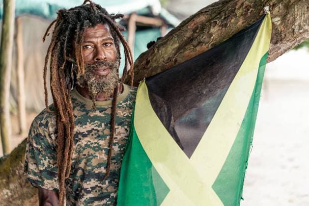 African American bearded male with dreadlocks holding Jamaica flag near tree Copyright: xVictorxBorderax Model Released