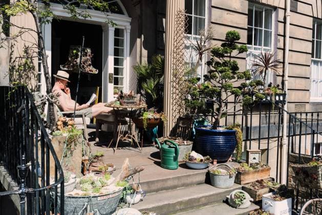 IMAGO Nature: Unsere Erde, Umweltvertr?gliche Herausforderungen, Recycling Man reading newspaper on porch with creative plants and trees in boxes and old utensil, Scotland Copyright: xVictorxBorderax Model Released