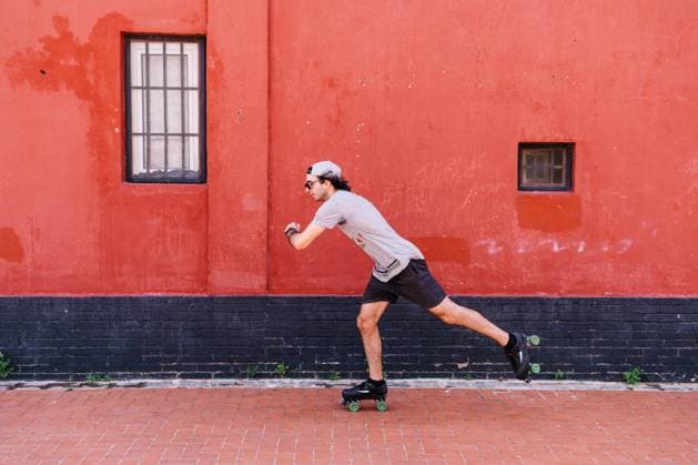 IMAGO Creative: Sport in der Stadt Side view of active stylish male in roller skates skating along street near red building while entertaining at weekend in summer Copyright: xVictorxGonzalezx Model Released