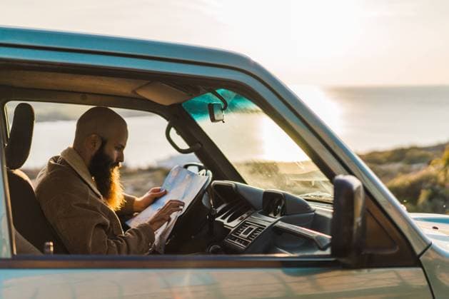 IMAGO Creative: Kulturelle Folgen der Pandemie: Gesundheitsbewu?tsein und Alleinsein Side view of adult bearded man resting in the car and reading map at the seaside. Copyright: xx Model Released