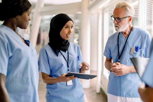 Confident female nurse with digital tablet talking to coworkers in hospital Sweden, Stockholm, model released, property released Copyright: xMaskotx , MA83363