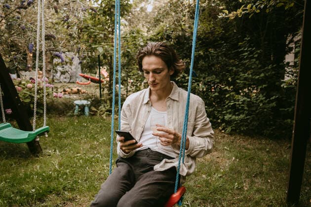 Contemplating man with drink using smart phone while sitting on swing in yard Sweden, Stockholm, model released, property released Copyright: xMaskotx , MA83415