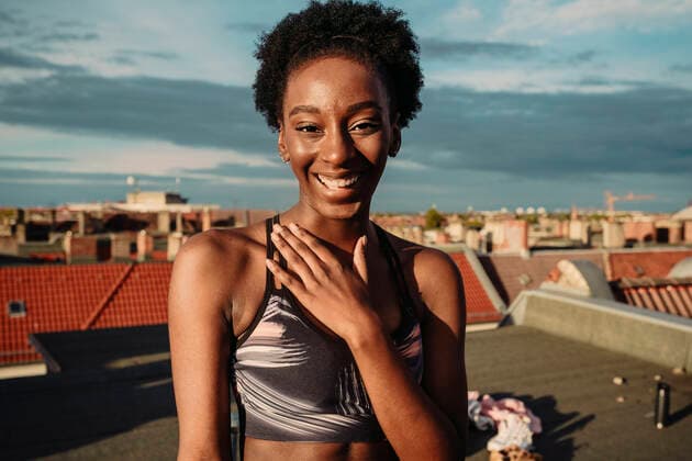 IMAGO Creative: Clickbait, Sport und Fitness Portrait of happy female in sports clothing standing on rooftop during sunrise Germany, Berlin, model released, property released Copyright: xMaskotx , MA83560