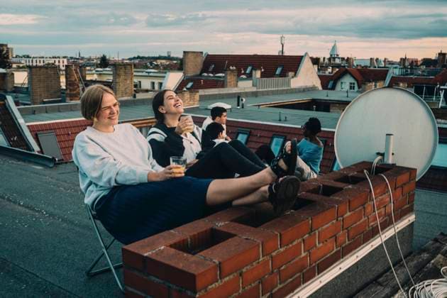 IMAGO Creative, Lifestyle, Leben in einer Wohngemeinschaft, WG IMAGO Kreativ: Urbane Kultur - Sommer auf den Dächern Smiling female talking to friend while enjoying drink on building terrace Germany, Berlin, model released, property released Copyright: xMaskotx , MA83600