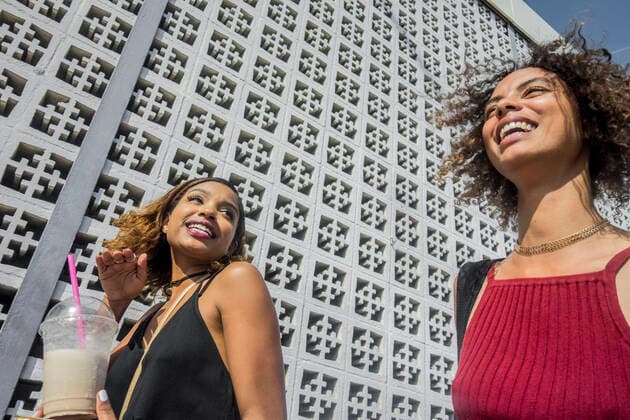 Cheerful young female friends walking by wall on sunny day model released Symbolfoto AJOF00616