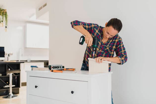 Craftsperson using electric screwdriver while standing by cabinet at home model released Symbolfoto property released DMGF00402