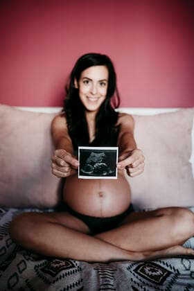 Mid adult pregnant woman showing ultrasound scan while sitting on bed at home model released Symbolfoto property released EBBF01607
