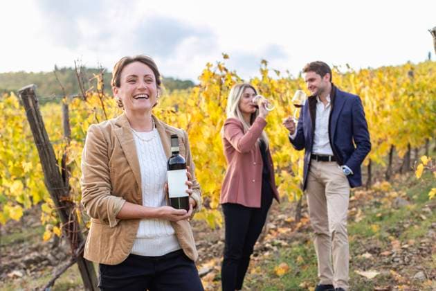 Female entrepreneur holding wine bottle while clients standing and drinking during autumn model released Symbolfoto property released EIF00350